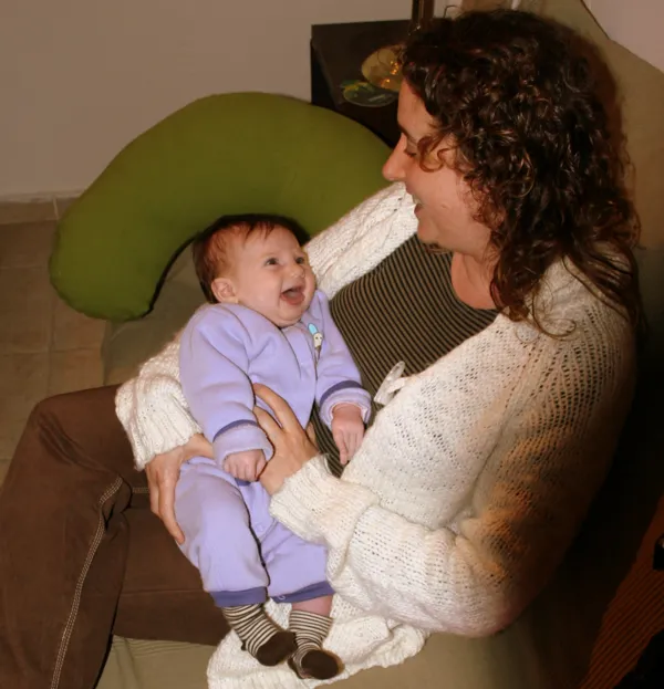 הגר מחזיקה תינוקת מחייכת על הברכיים בביקור בית אחרי לידה