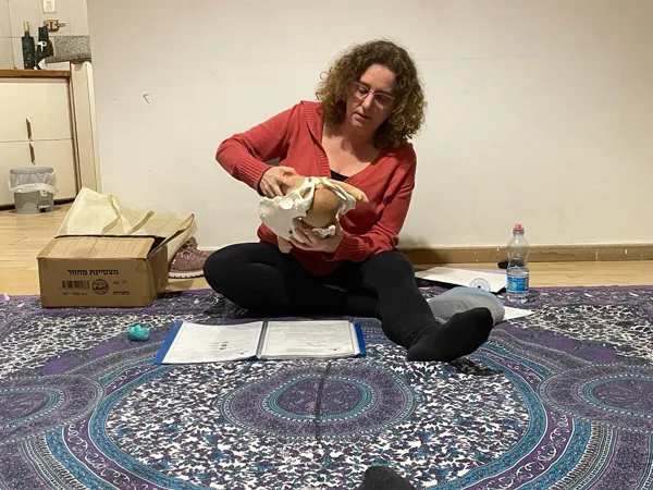 הגר יושבת על שטיח בסטודיו ומדגימה עם דגם של אגן